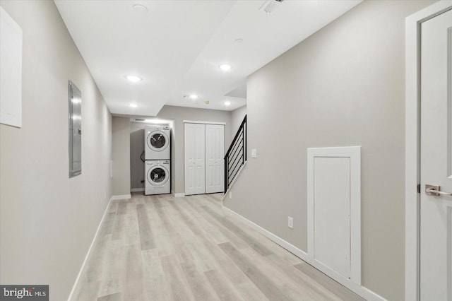 hall featuring electric panel, stacked washer / dryer, and light hardwood / wood-style flooring