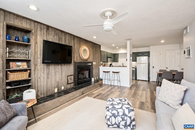 living room with ceiling fan, wood walls, a textured ceiling, and hardwood / wood-style floors