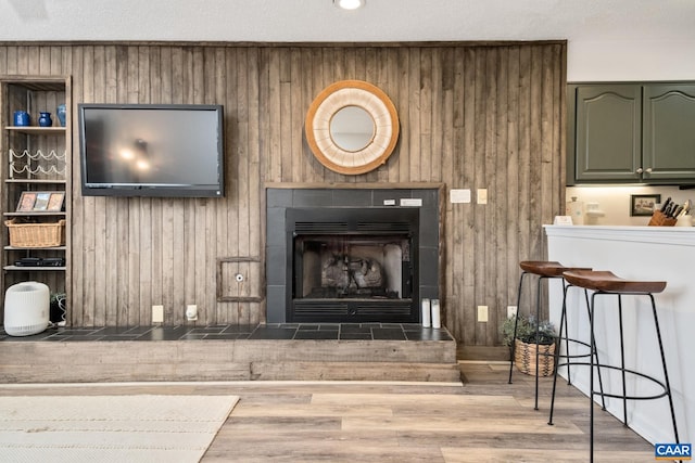 interior details featuring a textured ceiling, hardwood / wood-style flooring, a tile fireplace, and wood walls