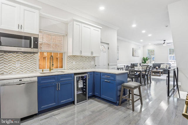 kitchen with stainless steel appliances, beverage cooler, sink, blue cabinetry, and white cabinetry