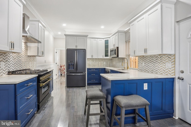 kitchen featuring white cabinets, blue cabinetry, wall chimney exhaust hood, and appliances with stainless steel finishes