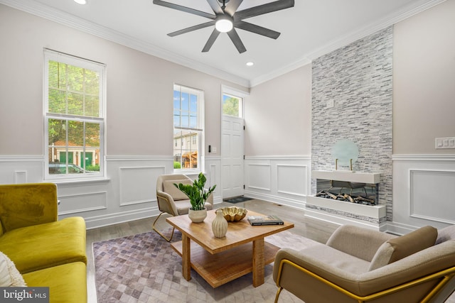 living room with a stone fireplace, wood-type flooring, ceiling fan, and crown molding