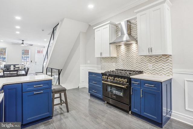 kitchen with white cabinetry, blue cabinetry, wall chimney range hood, light wood-type flooring, and stainless steel range