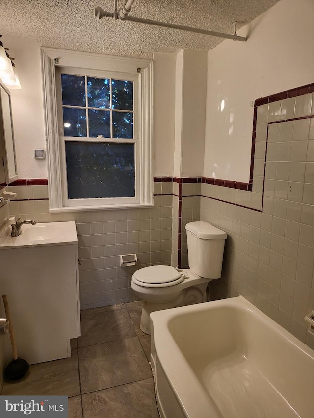 bathroom with a bathtub, vanity, toilet, a textured ceiling, and tile walls