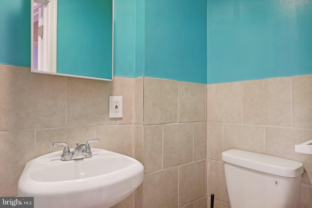 bathroom featuring toilet, sink, and tile walls