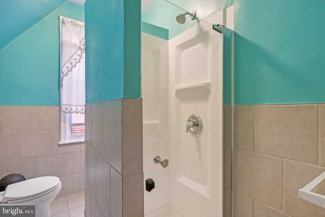 bathroom with toilet, a shower, tile patterned flooring, and tile walls