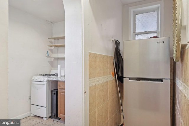 kitchen with white range with gas stovetop, tile walls, stainless steel fridge, and light tile patterned floors