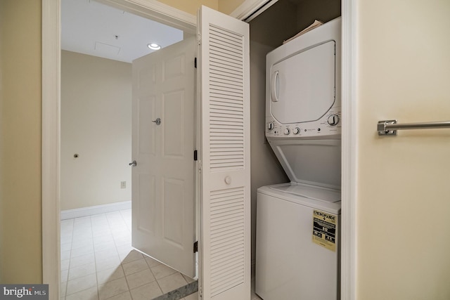 laundry area with stacked washer / drying machine and light tile patterned flooring