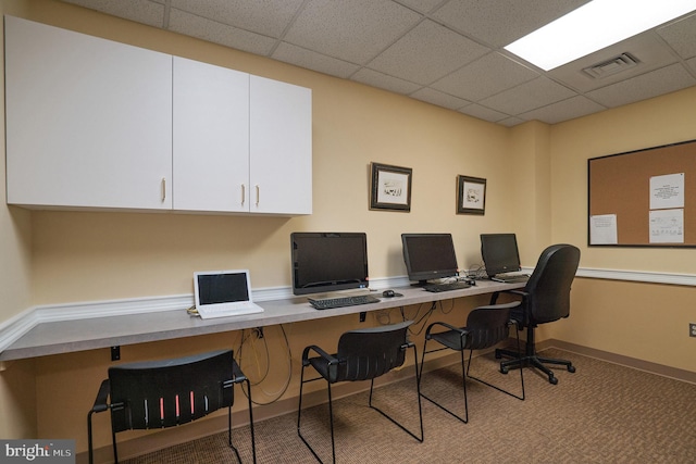 carpeted home office with a drop ceiling and built in desk