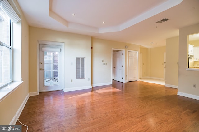 empty room with a wealth of natural light, hardwood / wood-style floors, and a raised ceiling