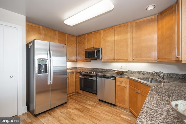 kitchen with sink, stainless steel appliances, light hardwood / wood-style floors, and dark stone countertops