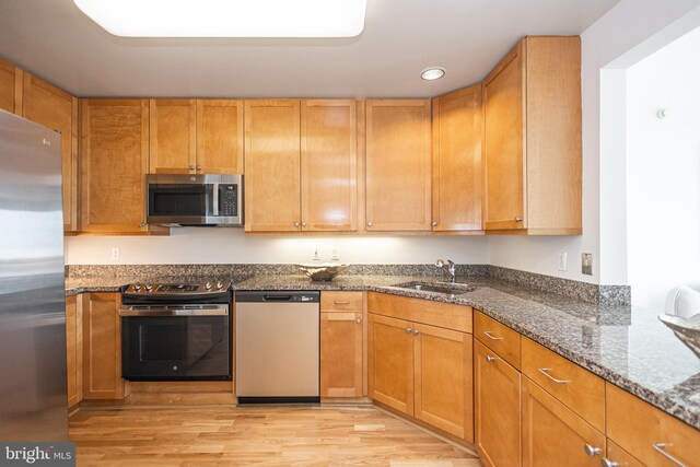 kitchen with dark stone counters, stainless steel appliances, sink, and light wood-type flooring