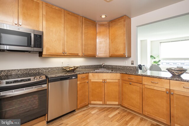 kitchen with appliances with stainless steel finishes, dark stone countertops, sink, and light hardwood / wood-style floors