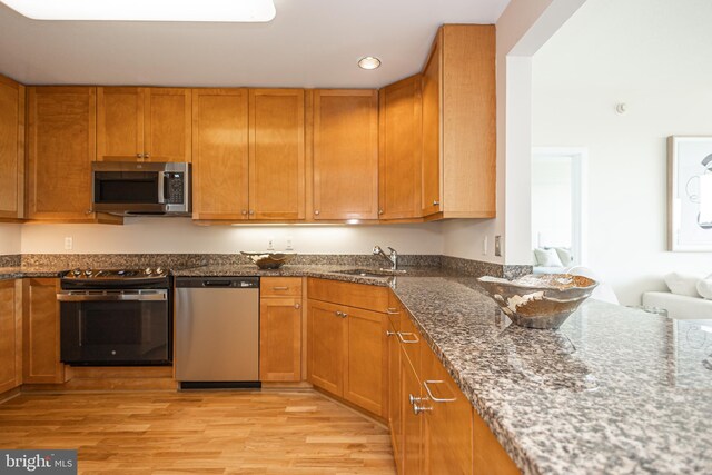 kitchen with sink, stainless steel appliances, light hardwood / wood-style floors, and dark stone countertops