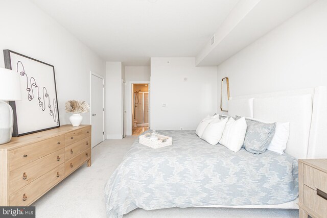 bedroom with ensuite bathroom and light colored carpet