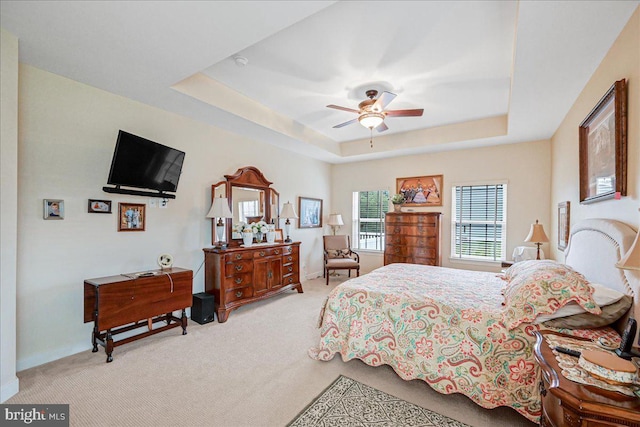 carpeted bedroom with a raised ceiling and ceiling fan