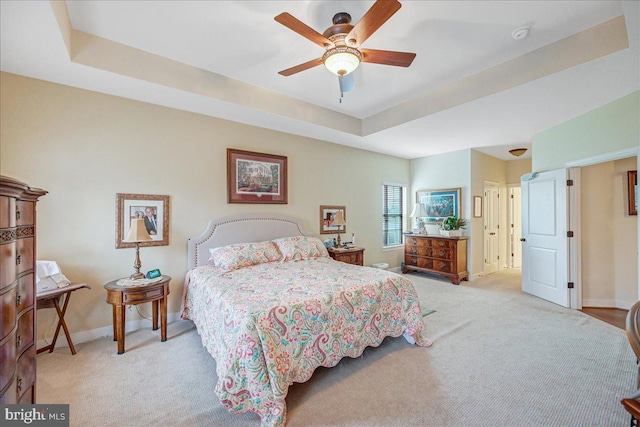 carpeted bedroom with a raised ceiling and ceiling fan