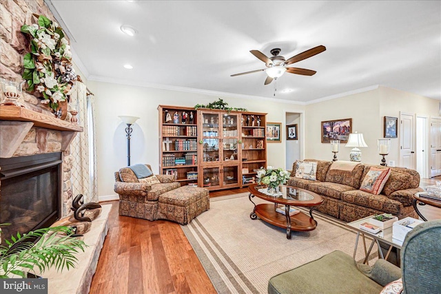 living room featuring hardwood / wood-style floors, a stone fireplace, crown molding, and ceiling fan