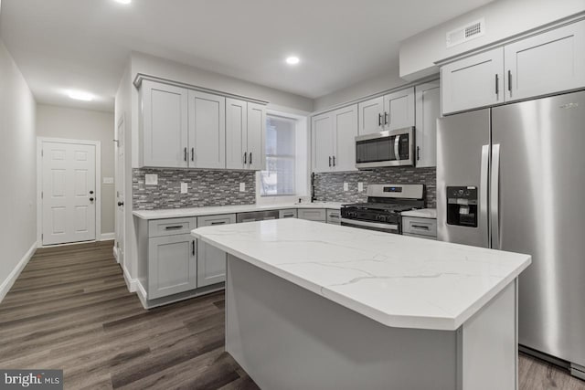 kitchen with light stone countertops, dark wood-type flooring, appliances with stainless steel finishes, and a kitchen island