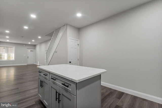 kitchen with gray cabinets, a kitchen island, light stone counters, and dark hardwood / wood-style flooring