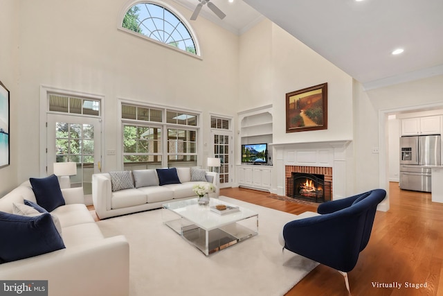 living room featuring a high ceiling, a fireplace, light wood-type flooring, and a healthy amount of sunlight