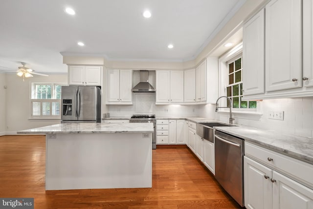 kitchen featuring a healthy amount of sunlight, appliances with stainless steel finishes, sink, a center island, and wall chimney exhaust hood