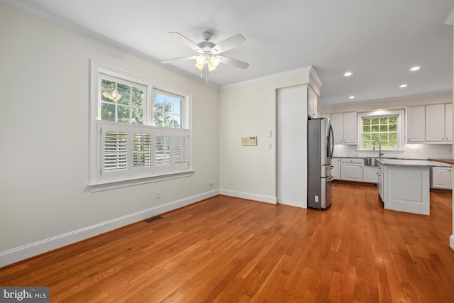 kitchen featuring ceiling fan, light hardwood / wood-style floors, white cabinets, crown molding, and stainless steel refrigerator