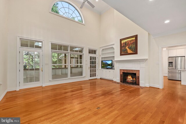 unfurnished living room featuring light hardwood / wood-style flooring, a brick fireplace, a towering ceiling, and plenty of natural light