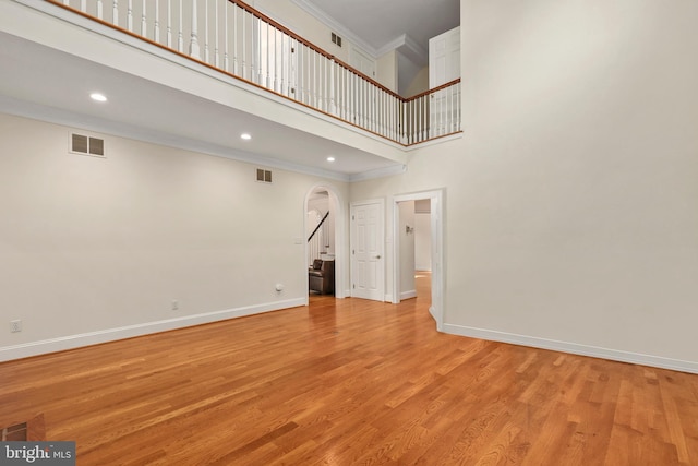 unfurnished living room with crown molding, light hardwood / wood-style floors, and a towering ceiling