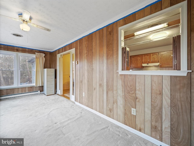 spare room featuring baseboard heating, crown molding, carpet, and wood walls