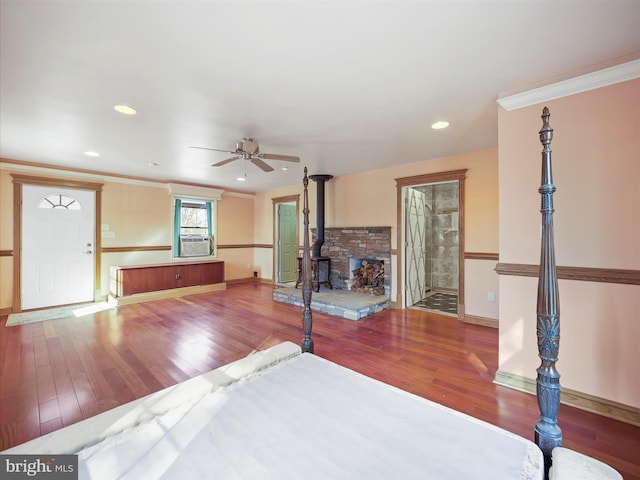 unfurnished living room featuring crown molding, ceiling fan, wood-type flooring, and a wood stove