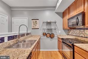 kitchen featuring black appliances, a sink, brown cabinetry, and light wood-type flooring