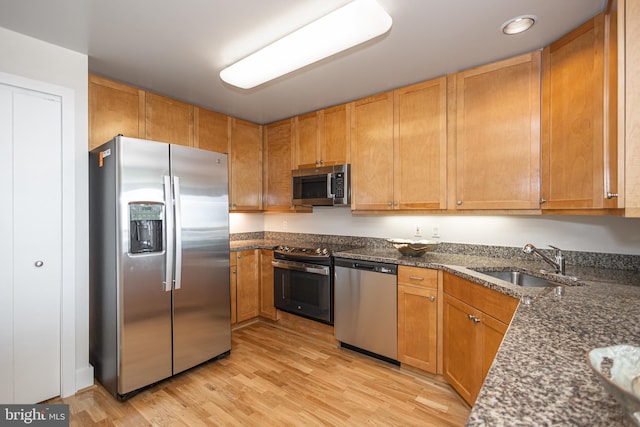 kitchen with dark stone counters, appliances with stainless steel finishes, sink, and light wood-type flooring