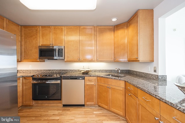 kitchen featuring appliances with stainless steel finishes, dark stone countertops, sink, and light wood-type flooring