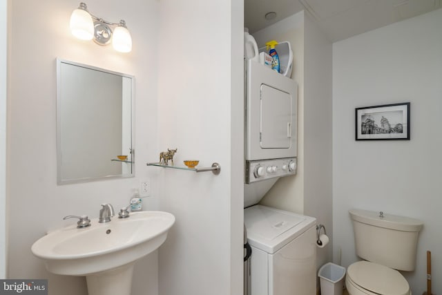 bathroom featuring stacked washer / drying machine, sink, and toilet