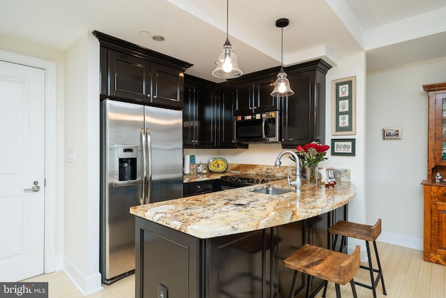 kitchen with appliances with stainless steel finishes, light hardwood / wood-style flooring, sink, pendant lighting, and light stone counters