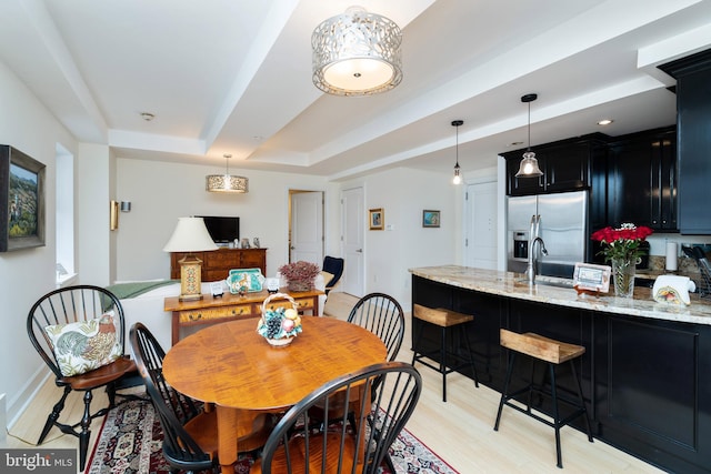 dining space featuring light hardwood / wood-style flooring, sink, and a raised ceiling