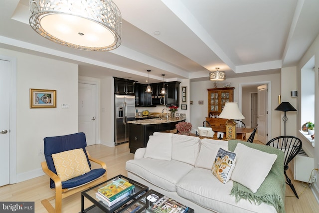 living room with a raised ceiling, sink, and light wood-type flooring