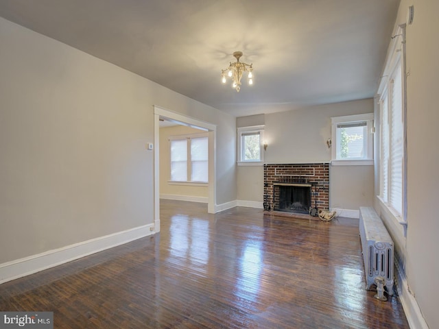 unfurnished living room featuring dark hardwood / wood-style flooring, radiator heating unit, a notable chandelier, and a brick fireplace