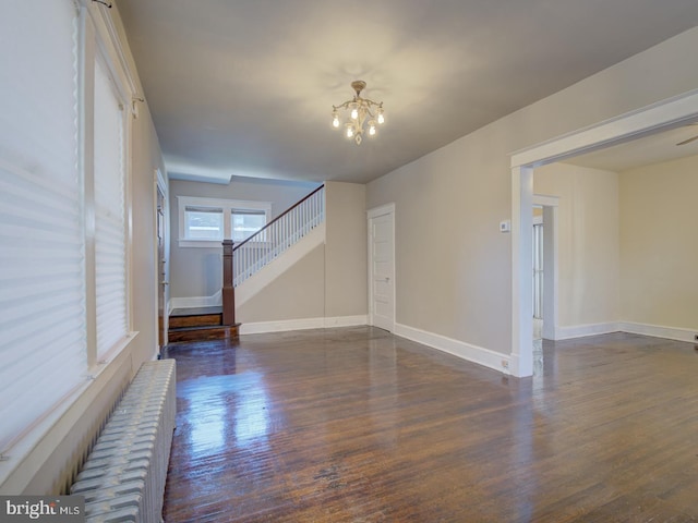 unfurnished living room with a notable chandelier and dark hardwood / wood-style floors