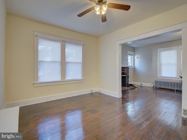 spare room featuring dark hardwood / wood-style flooring, radiator, ceiling fan, and a fireplace