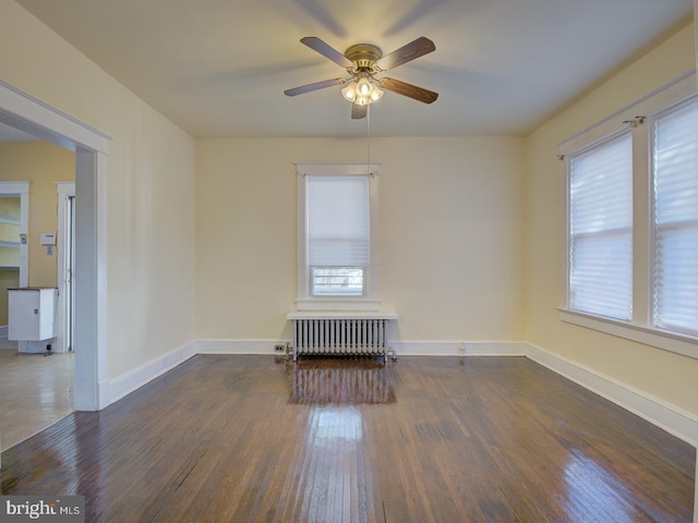 spare room with dark wood-type flooring, radiator, and ceiling fan