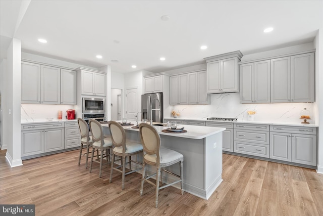 kitchen featuring gray cabinets, stainless steel appliances, a kitchen bar, and light wood-type flooring