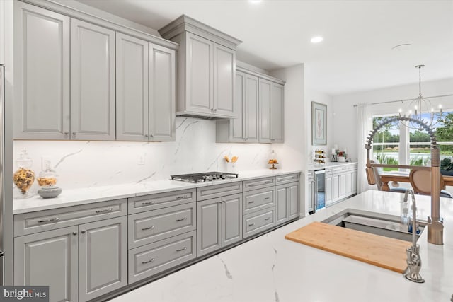 kitchen with gray cabinetry, hanging light fixtures, stainless steel gas stovetop, decorative backsplash, and an inviting chandelier