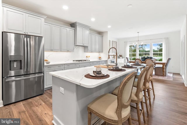 kitchen with appliances with stainless steel finishes, wood-type flooring, a center island with sink, and hanging light fixtures