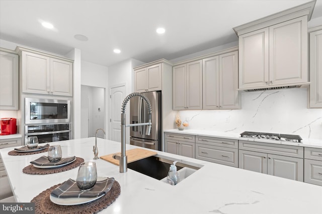 kitchen with light stone countertops, gray cabinetry, stainless steel appliances, and backsplash