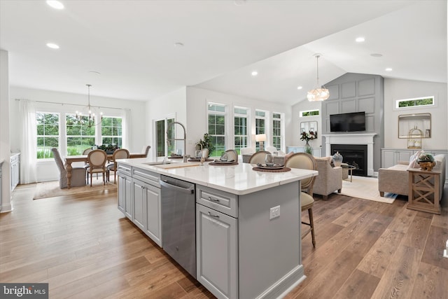 kitchen with lofted ceiling, a center island with sink, stainless steel dishwasher, light hardwood / wood-style flooring, and gray cabinets