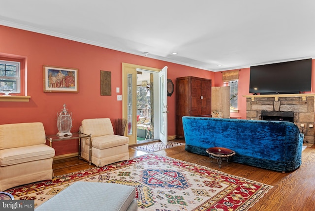 living room featuring crown molding, a stone fireplace, hardwood / wood-style flooring, and plenty of natural light