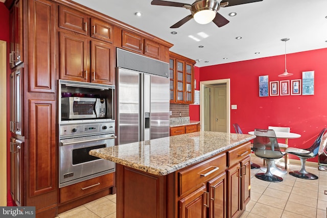 kitchen featuring ceiling fan, appliances with stainless steel finishes, light tile patterned floors, a kitchen island, and decorative light fixtures