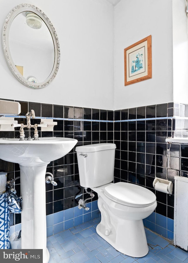 bathroom with toilet, tile patterned floors, and tile walls